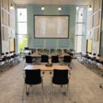Bright, spacious conference room featuring multiple workstations, AV technology, and a large central screen for professional meetings.