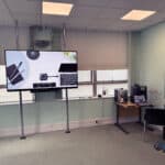 Office meeting room with large display screen, laptop, coffee machine, and professional workspace setup.